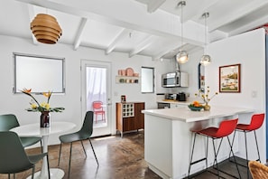 A modern kitchen with a central island, a dining area with chairs, and a kitchen counter with a microwave and toaster. - Deluxe King Studio in Boutique Hotel | The Rosalie (Palm Springs)