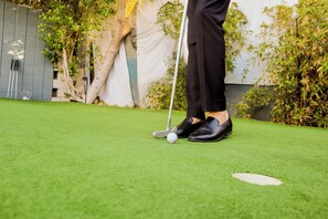 Eine Person steht auf künstlichem Rasen mit einem Golfball und Schläger in der Nähe eines weißen Lochs.