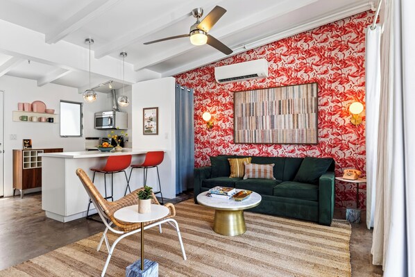 A modern living room with a green sofa, a round coffee table, and a dining area with red chairs. - Deluxe King Studio in Boutique Hotel | The Rosalie (Palm Springs)