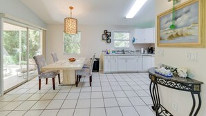 Una cocina moderna con armarios blancos, un comedor con mesa y sillas, y vistas al exterior a través de grandes ventanales.