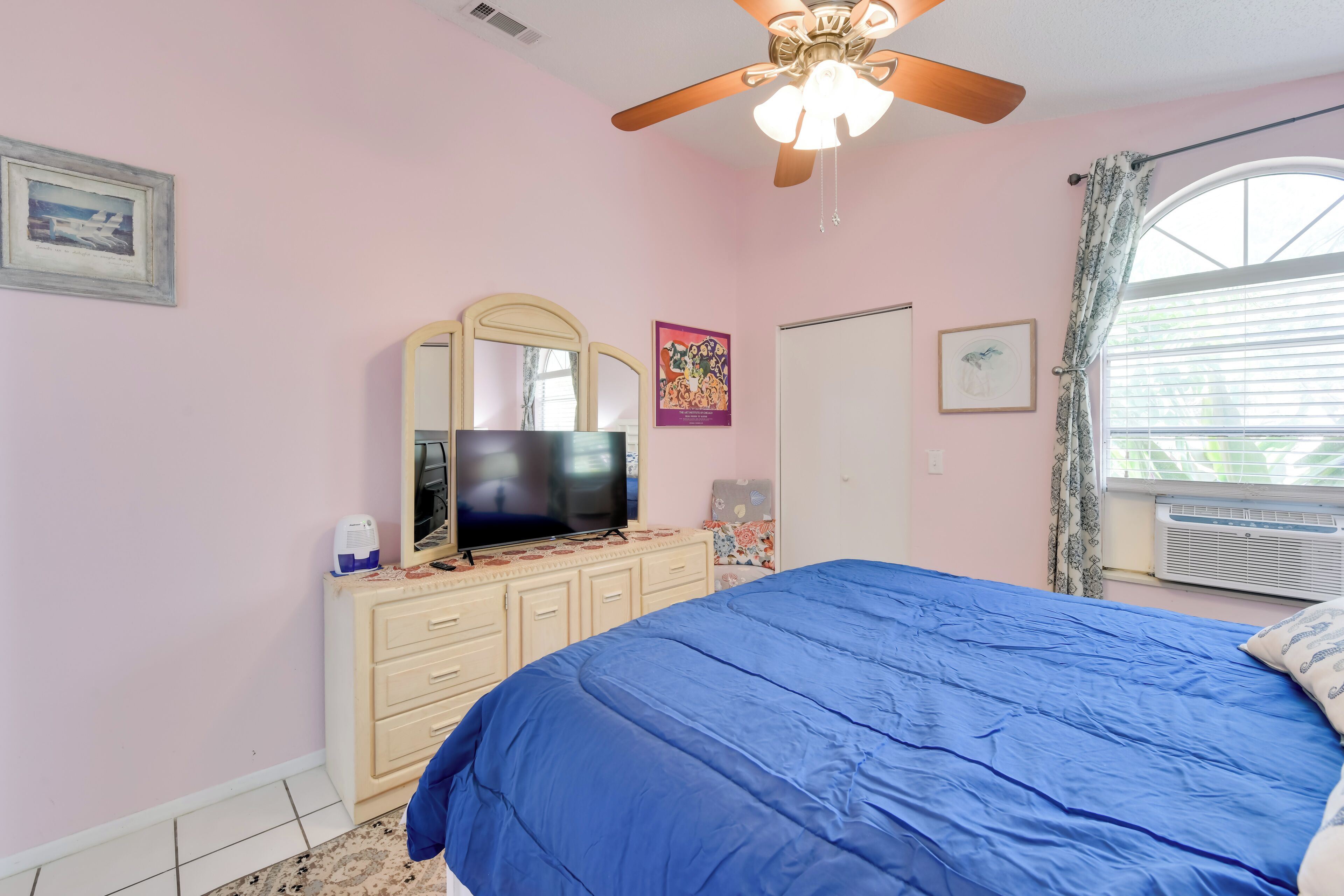 A bedroom with a bed, a dresser, a television, and a ceiling fan.