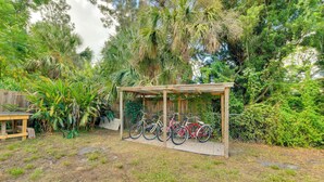 A covered bike rack in a garden with various plants and a wooden table.