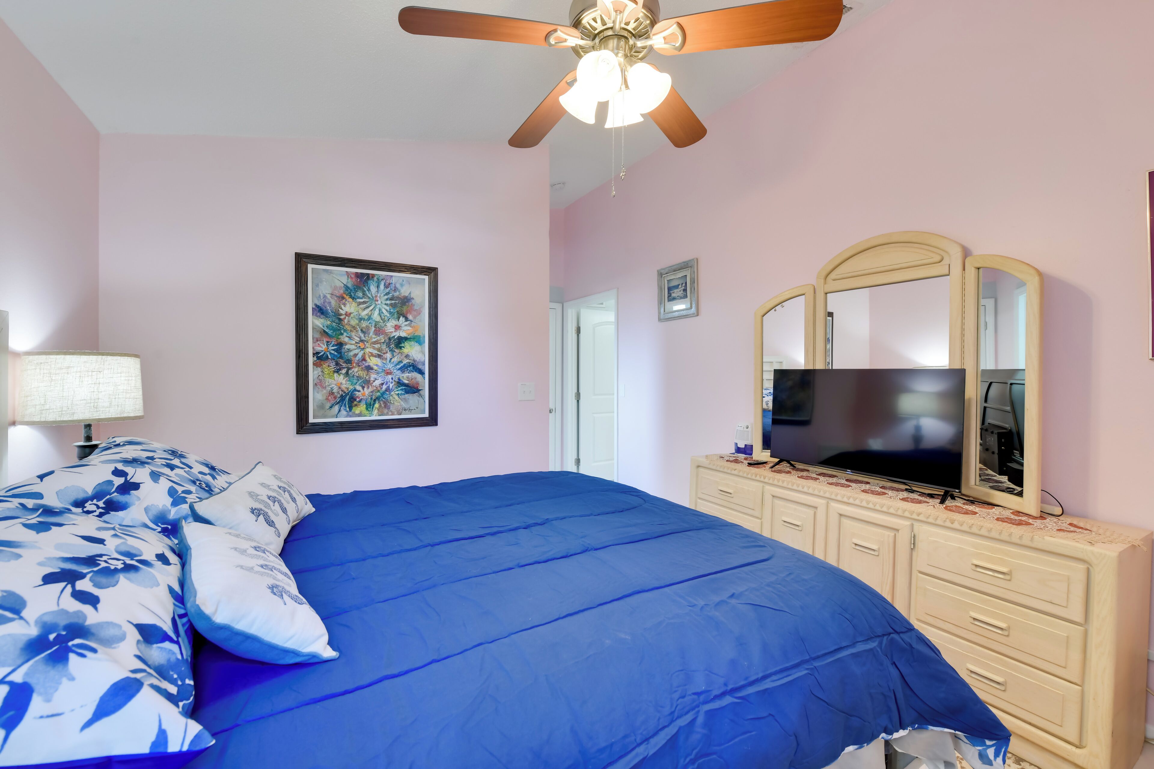 Une chambre à coucher avec un lit, un ventilateur de plafond, une commode, un téléviseur et un tableau encadré accroché au mur.