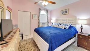 A bedroom with a bed, a ceiling fan, a dresser, a TV, and a window with curtains.