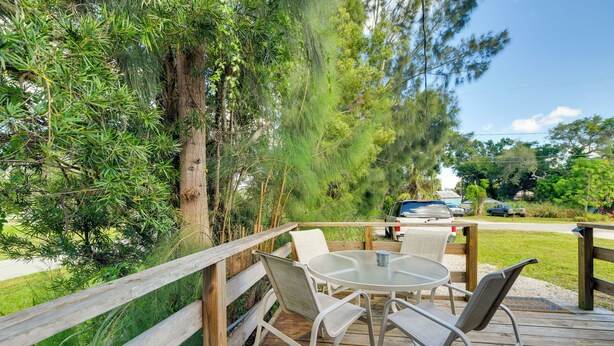 A wooden deck with a table and chairs, surrounded by trees and a view of a road with cars.