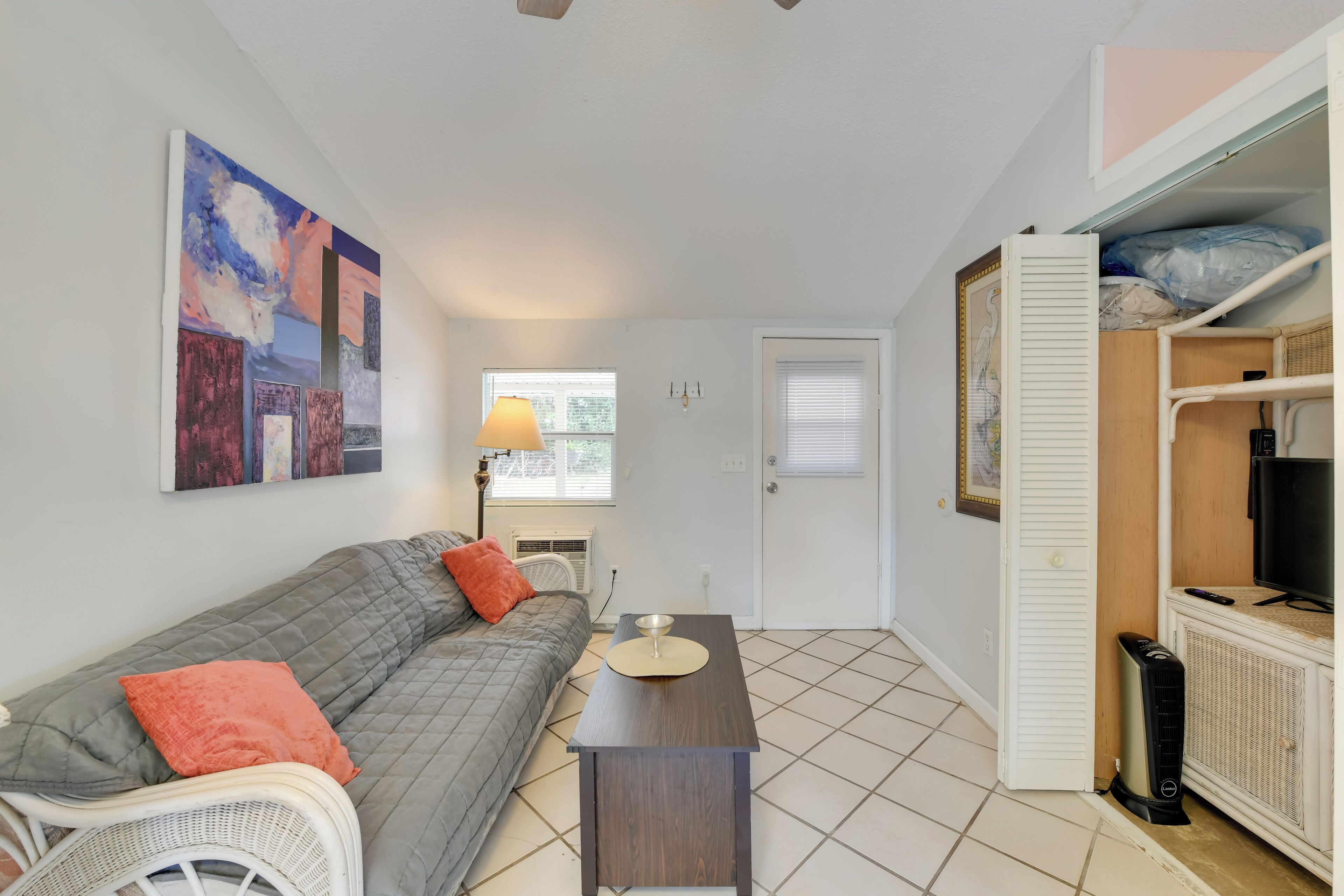Un espace de vie compact comprenant un canapé, une petite table, un radiateur blanc et un téléviseur posé sur un meuble.
