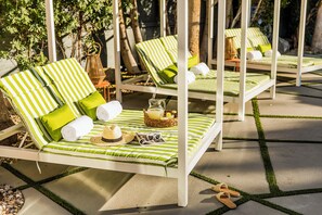 Une rangée de chaises longues blanches, dotées de coussins à rayures vertes et blanches, est disposée sur une terrasse en béton bordée de gazon vert.