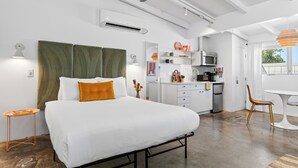 Ein modernes Schlafzimmer mit Bett, Deckenventilator, Klimaanlage und einer Küchenzeile im Hintergrund.
