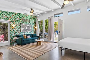 Un salon moderne avec un mur orné d’un motif vert, un canapé turquoise, une table basse et un grand lit.