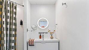 Ein Badezimmer mit Duschvorhang, Waschbecken mit Handtuch, Spiegel und einer Vase mit Blumen.