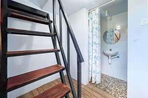 Una escalera con escalones de madera y barandillas negras que conduce a un baño con un lavabo blanco y un espejo redondo.