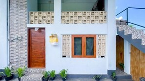 A two-story building with a wooden door, a window with a grid pattern, and a balcony with a stone wall. - Winy House (Bali)