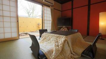 Een traditionele Japanse kamer met tatami vloeren, een bed belegd met tatami matten, een televisie en een schuifdeur naar een balkon.