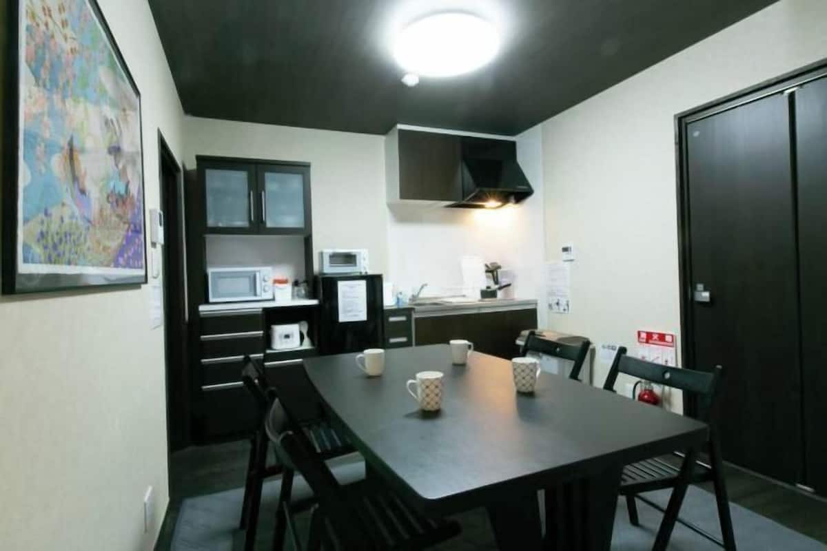 A compact kitchen with a microwave, stove, and cabinets, a dining table with chairs, and a dark door.