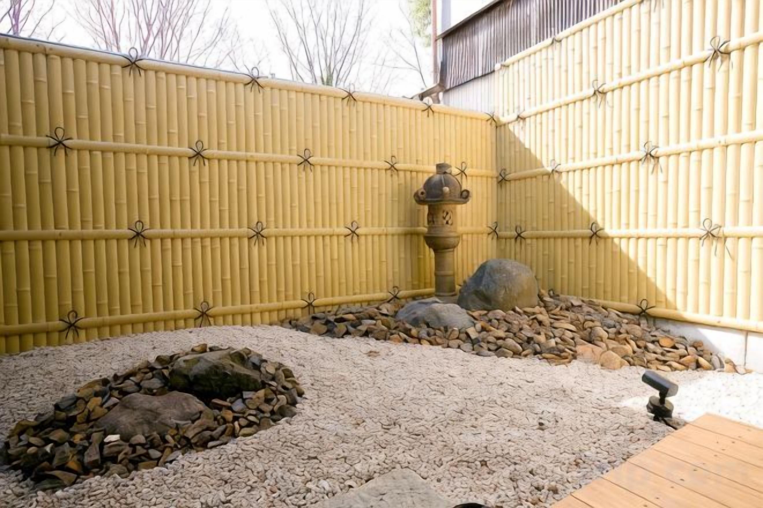 Una cerca de bambú, un elemento decorativo de piedra con agua y un área de grava con rocas.