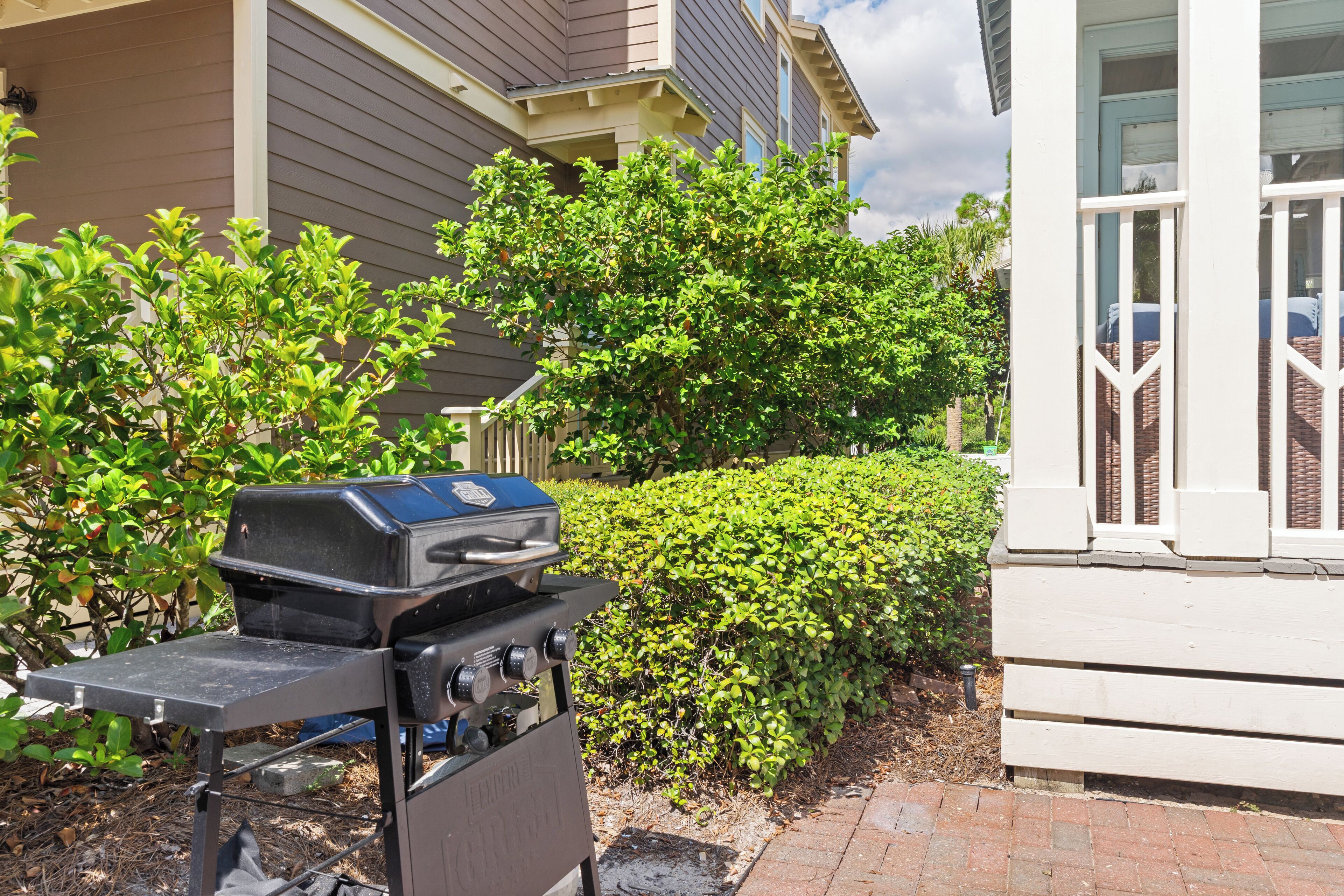 A barbecue grill in a residential area with a house and well-maintained bushes in the background.