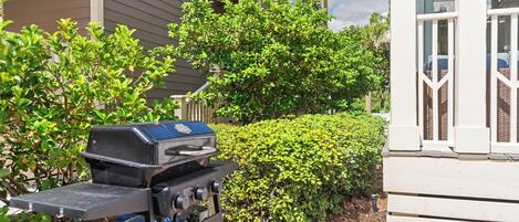 A barbecue grill in a residential area with a house and well-maintained bushes in the background.