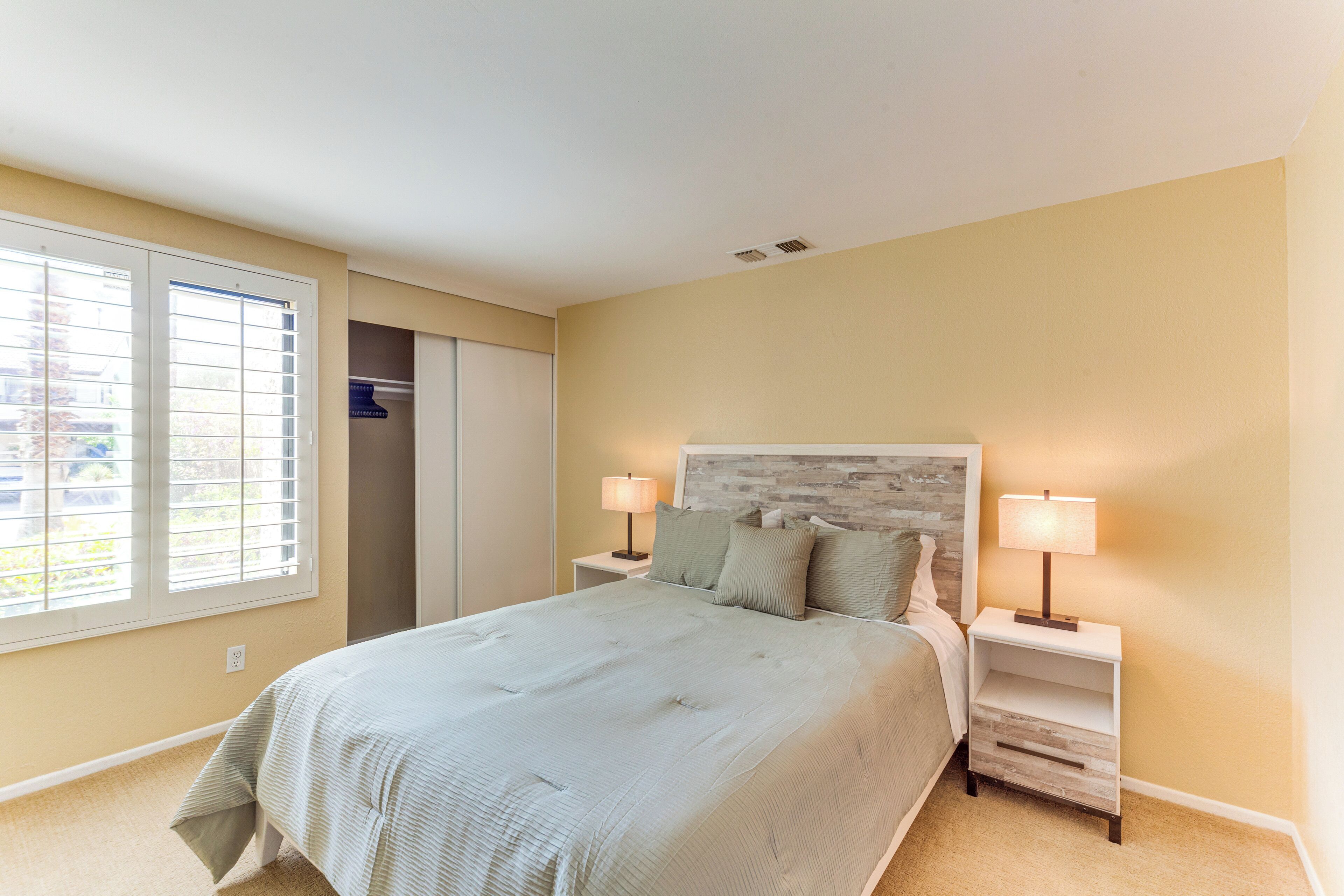 A bedroom with a bed, two bedside tables with lamps, a closet, and a window with blinds.