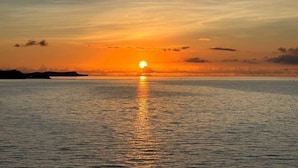 A sunset over a calm sea with a distant shoreline. - STARS (Kunigami District)