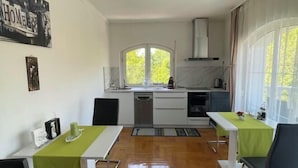 A compact kitchen with a large window, a dining area with two tables, and a view of greenery outside. - Meszko Park House Budapest (Budapest)