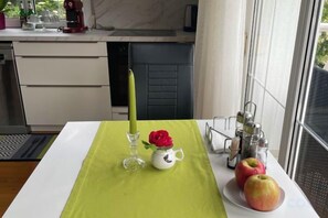 Una cucina con un tavolo apparecchiato per due, con un sottopiattino verde, una tazza bianca, una rosa rossa e due mele.