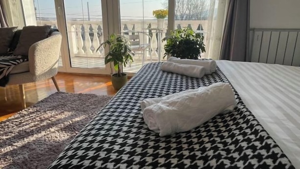 A hotel room with a large bed, a sofa, and a balcony with potted plants. - Meszko Park House Budapest (Budapest)