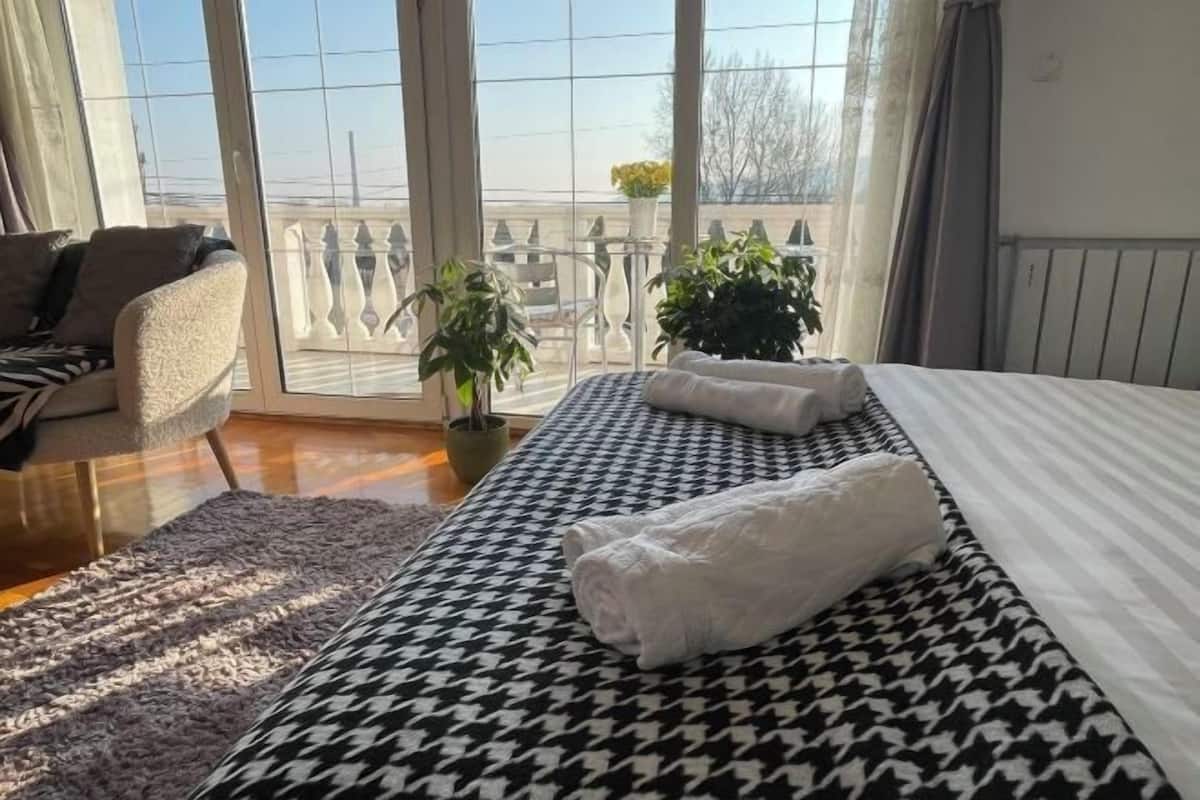 Una habitación de hotel con una cama grande, un sofá y un balcón con plantas en macetas.