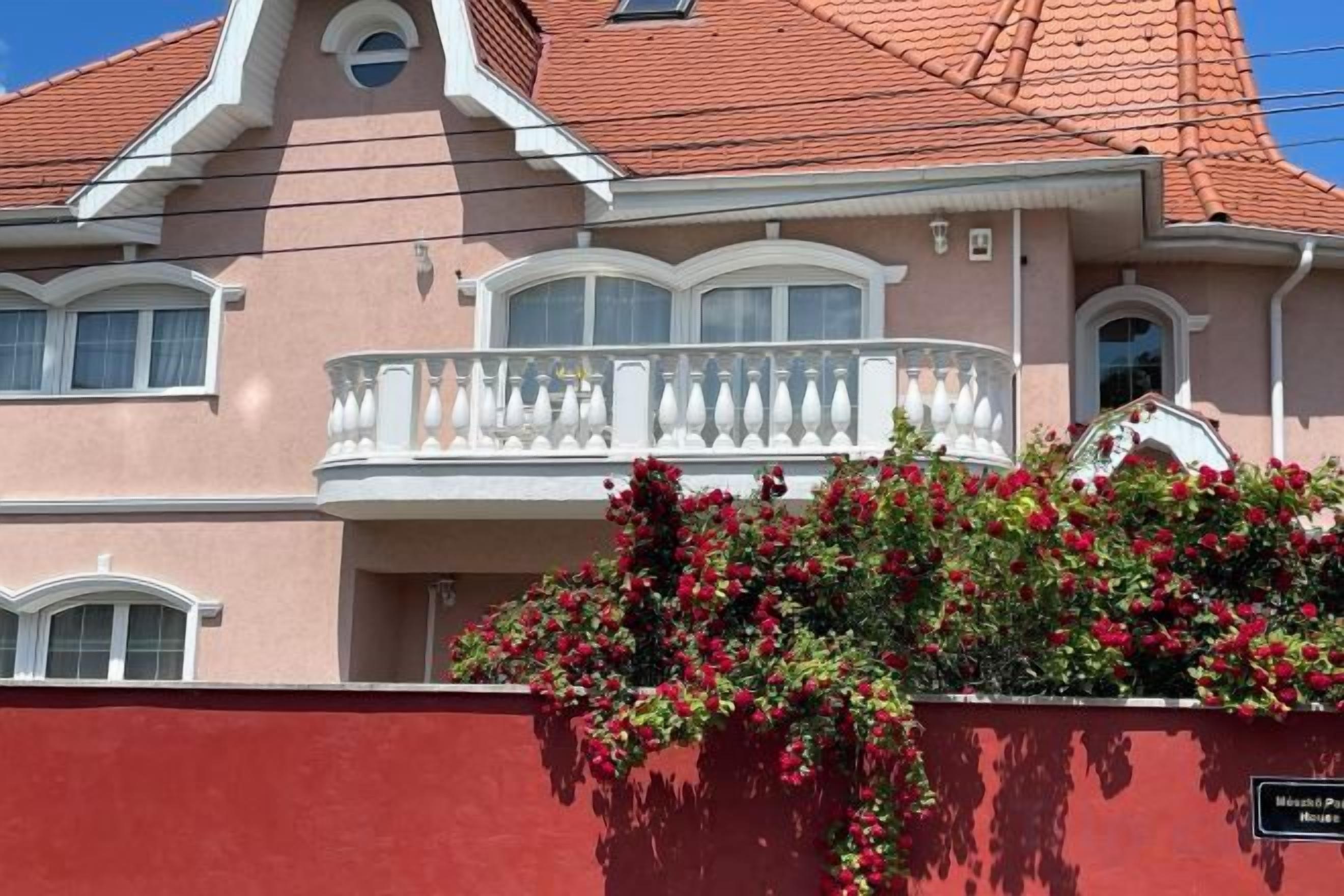A two-story building with a balcony and a red wall in front.