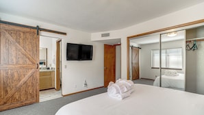 Ein Hotelzimmer mit einem großen Bett, einem an der Wand befestigten Fernseher, einer Schiebetür und einem Spiegel, der einen Teil des Raumes widerspiegelt.