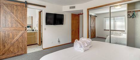 Une chambre d’hôtel avec un grand lit, un téléviseur fixé au mur, une porte coulissante et un miroir qui reflète une partie de la pièce.