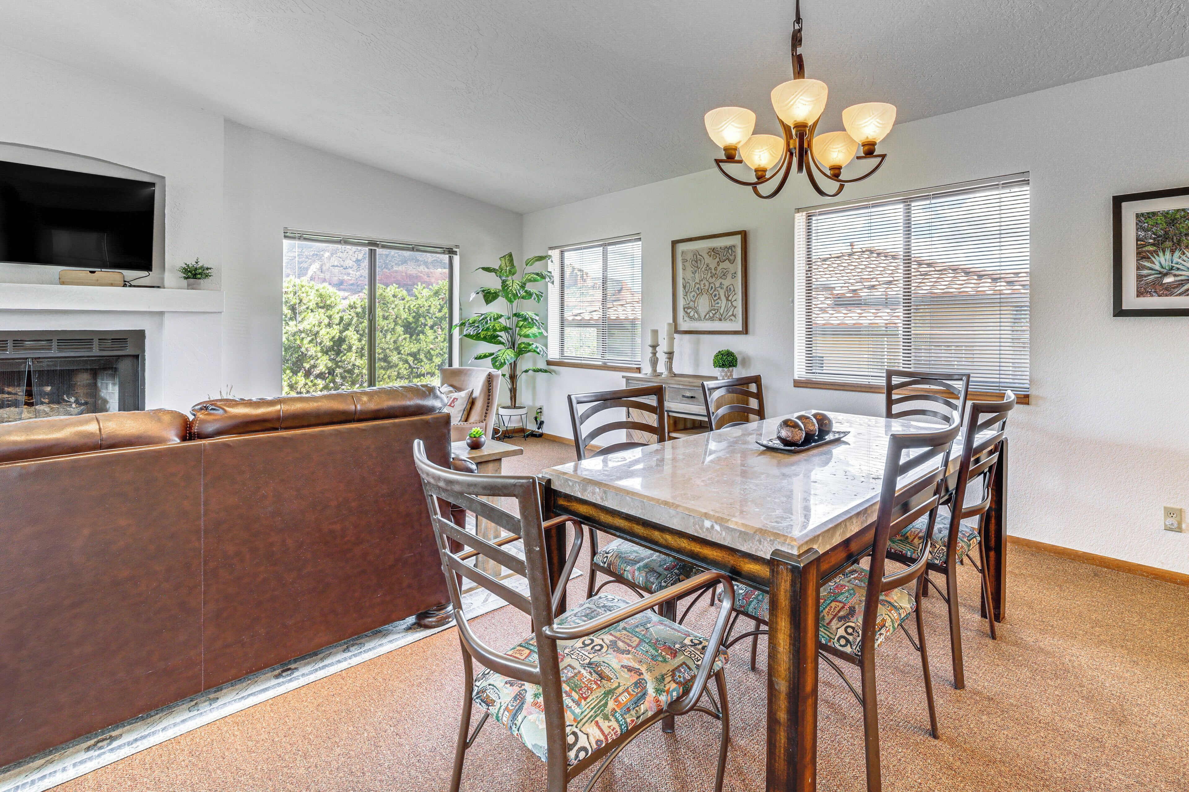 A dining area with a wooden table and chairs, a fireplace, and a large window with blinds.