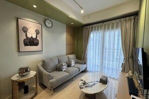 Una sala de estar con sofá, una mesa de centro, un reloj y un ventanal con cortinas.