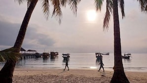 A beach with palm trees and boats in the background. - Island Boutique Koh Rong (Sihanoukville)