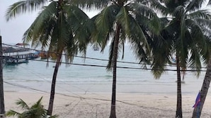 A beach with palm trees and a pier in the background. - Island Boutique Koh Rong (Sihanoukville)