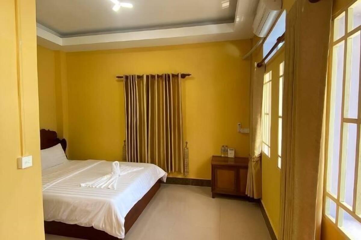A hotel room with a bed, a nightstand, a window with curtains, and a ceiling light.
