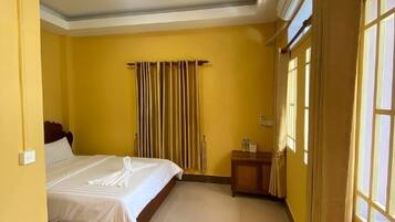 A hotel room with a bed, a nightstand, a window with curtains, and a ceiling light.