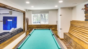 A pool table with a green felt surface, wooden benches, and a window with a view of trees. - Golf & Swim! Pine Mtn Club Retreat w/ Game Area (Pine Mountain Club)