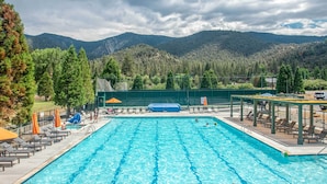 A swimming pool with lounge chairs and umbrellas, surrounded by a fence and trees, with mountains in the background. - Golf & Swim! Pine Mtn Club Retreat w/ Game Area (Pine Mountain Club)