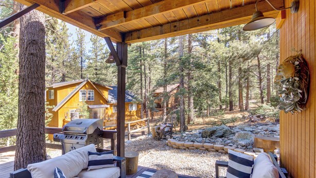 A covered outdoor seating area with a wooden deck, a grill, and a view of a cabin in a forested area. - Golf & Swim! Pine Mtn Club Retreat w/ Game Area (Pine Mountain Club)