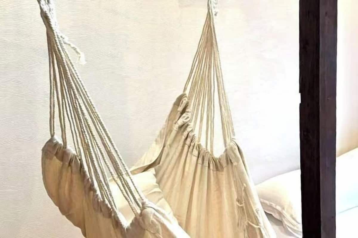 Eine Hängematte, die von der Decke hängt, ein Bett mit weißer Bettwäsche und eine Holzkonstruktion rechts.