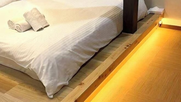 A neatly made bed with a white comforter and rolled towels, a wooden floor, and a wall-mounted light fixture. - JIA MING (Osaka)