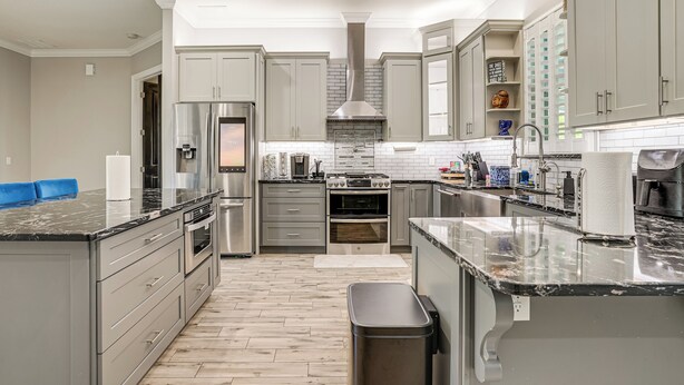 A modern kitchen with grey cabinets, stainless steel appliances, and a marble countertop.