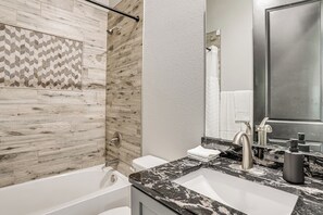 A modern bathroom with a bathtub, a shower, and a sink with a marble countertop.