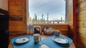 L’intérieur d’un chalet en bois, avec une table à manger dressée pour deux personnes, un réfrigérateur et une fenêtre donnant sur une forêt.