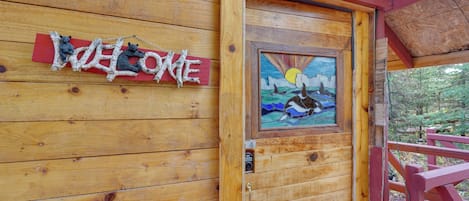 A wooden cabin with a 'Welcome' sign and a painting of a bear.