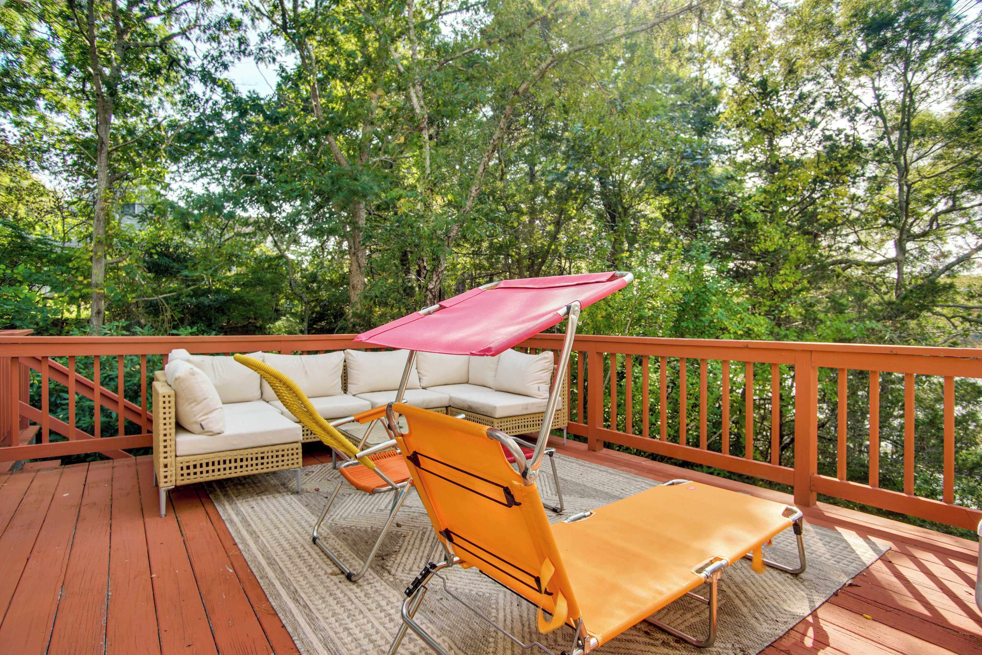 A deck with wicker furniture, including a sofa and two lounge chairs, one with a red canopy.