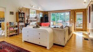 A spacious living room with a large white sofa, a fireplace, and a view of the outdoors through large windows.