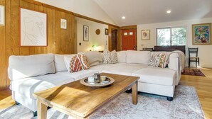 A living room with a large white sectional sofa, a wooden coffee table, and a dining area with a wooden table and chairs.