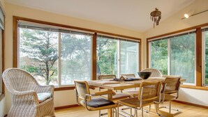A dining area with a table and chairs, large windows, and a wicker chair.