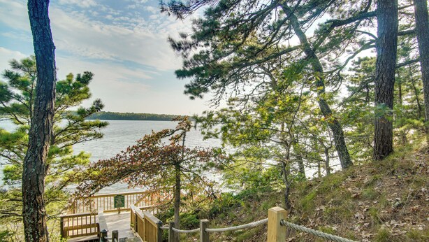 A wooden deck leading to a lake with a view of the water and surrounding trees.